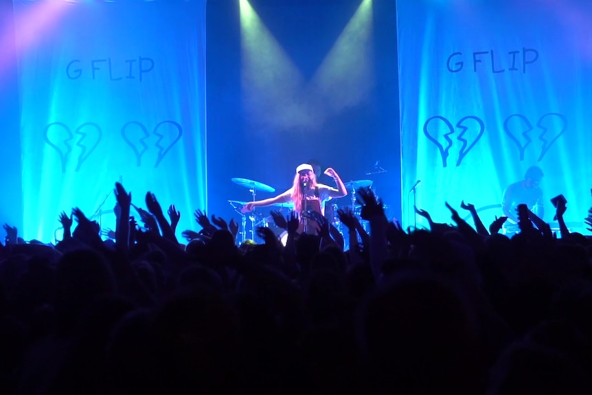 A musician sings on stage with blue lights and a crowd