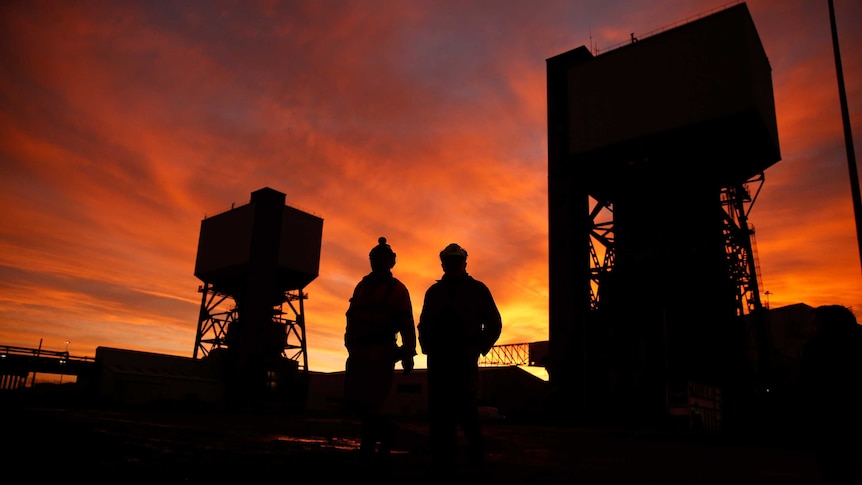 Two miners walking through a coal mine at sunset