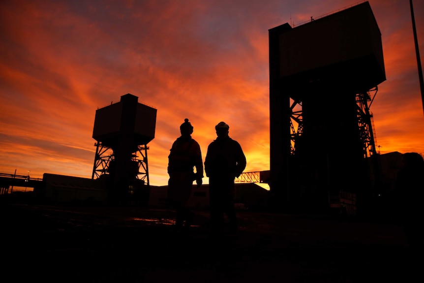 Two miners walking through a coal mine at sunset