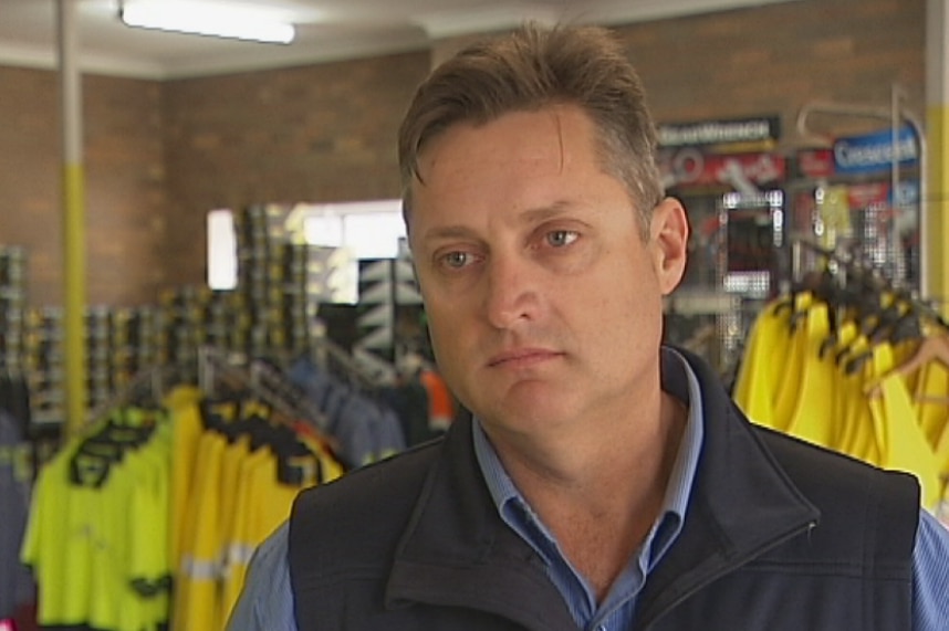 A man, with a serious expression, stands in a shop with high-viz shirts in the background.