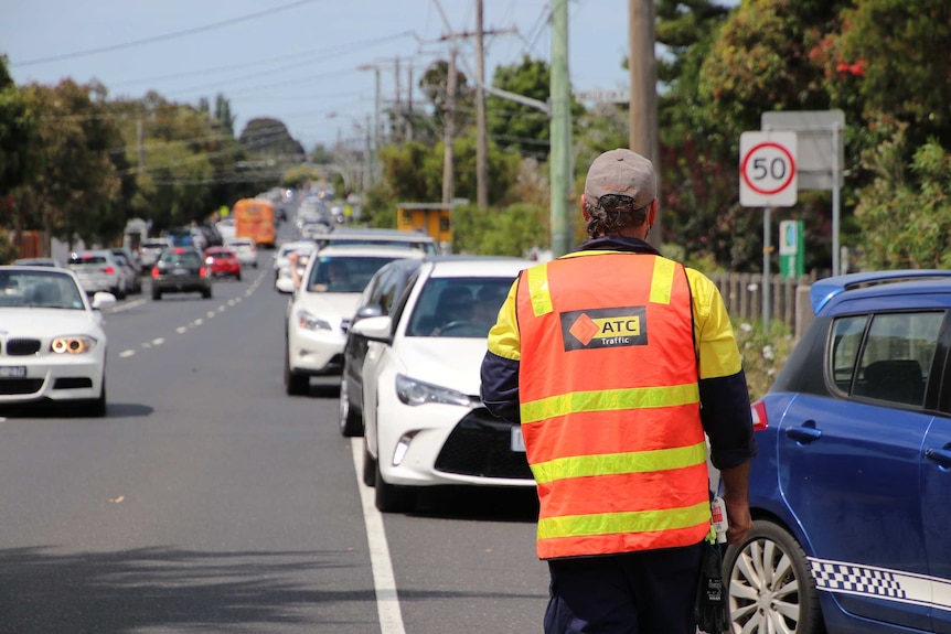 A traffic warden in an orange high-vis shirt directs traffic from a long queue.