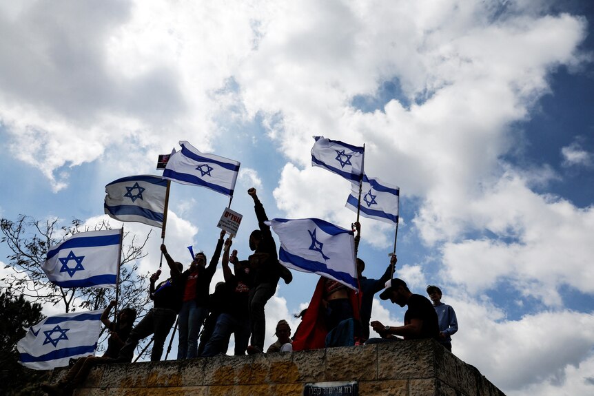 A group of protesters on a hill hold the Israeli flags.