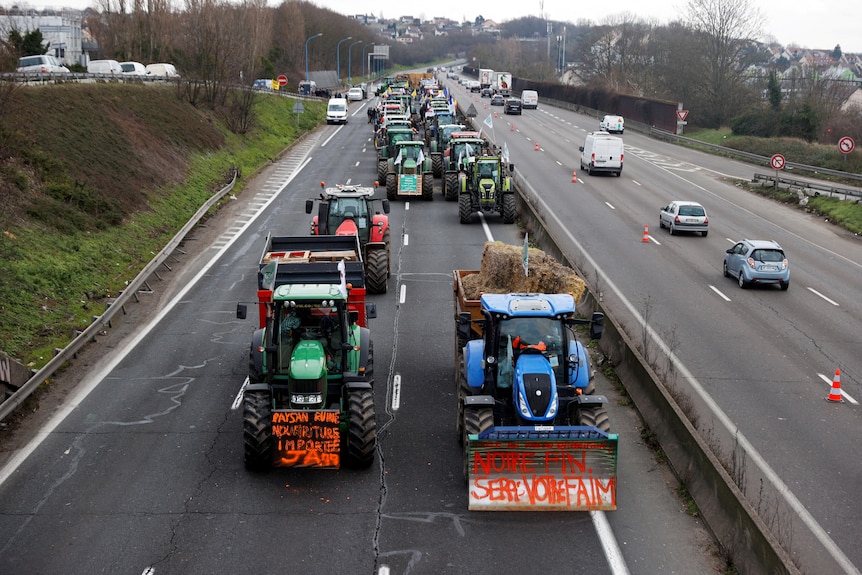 Tractors in two long rows on one side of a majpor highway.