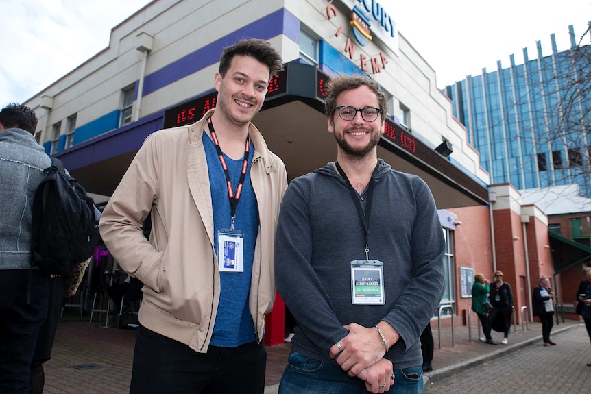 Two smiling men in their twenties outside a cinema building