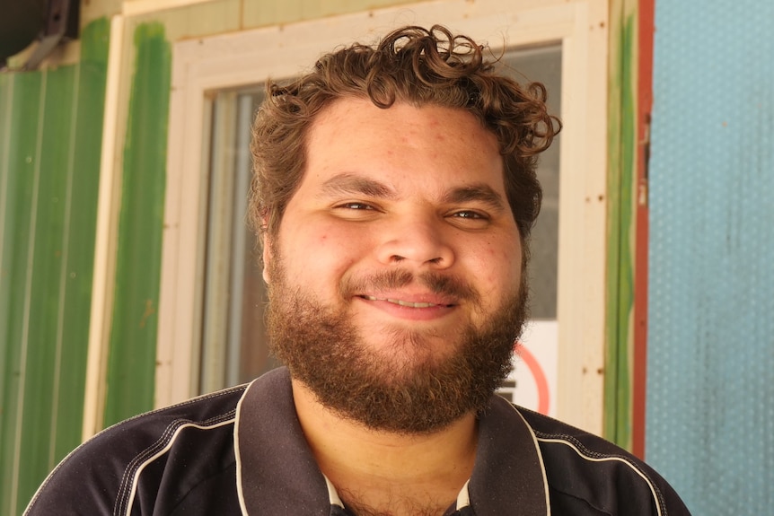 A young, dark-bearded Aboriginal man standing outside an outback radio studio