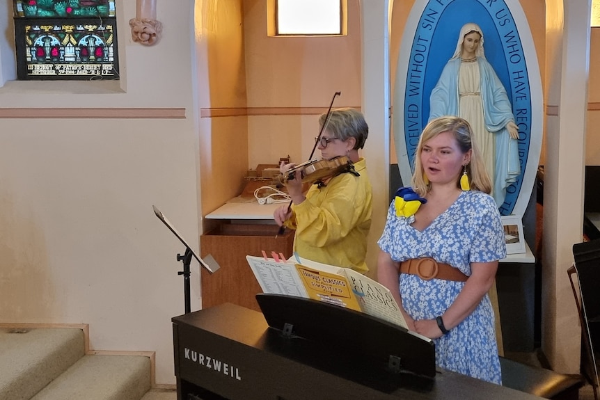 Woman standing next to a violinist in a church singing. 
