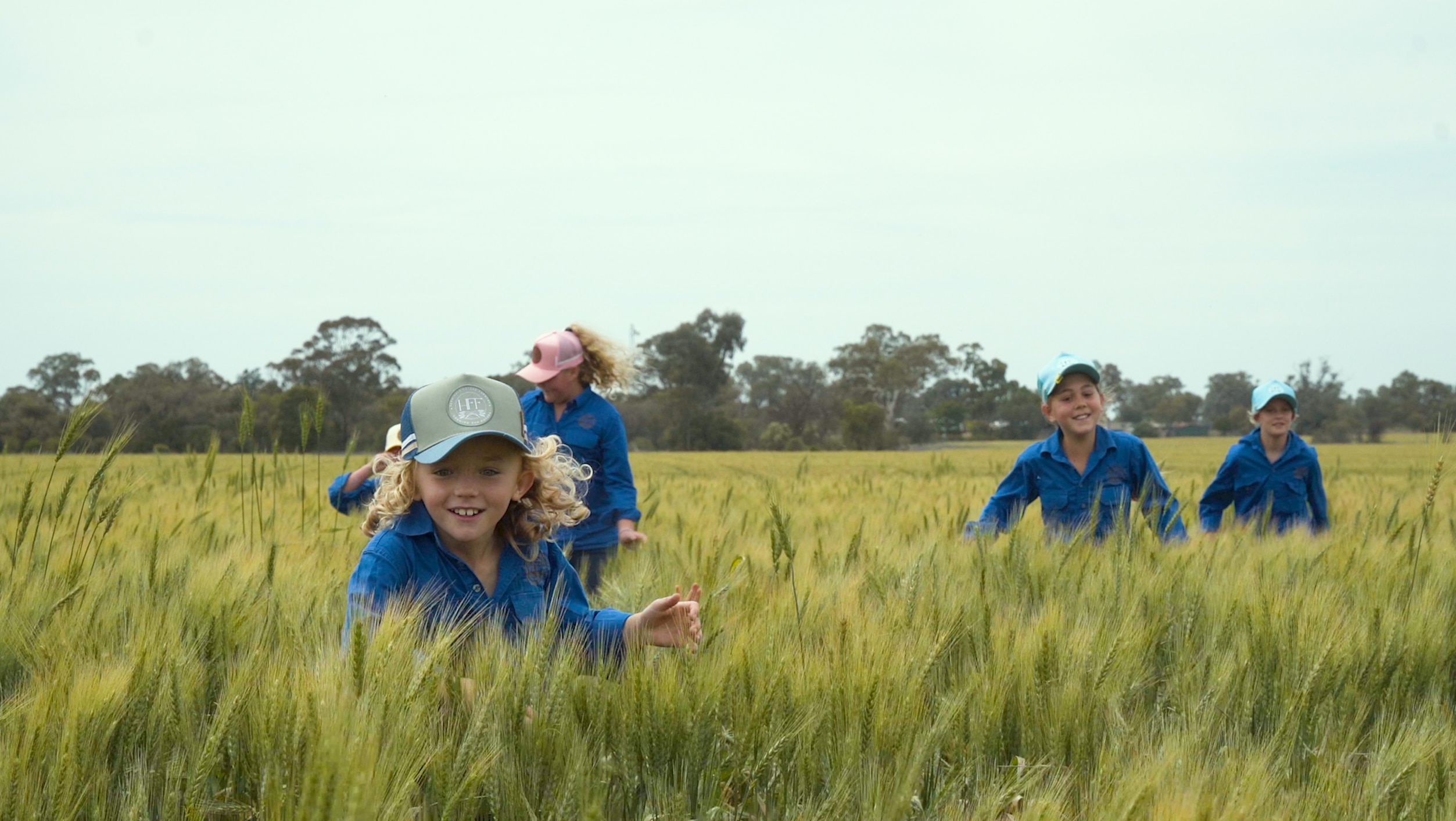 five primary school students run through a wheat field