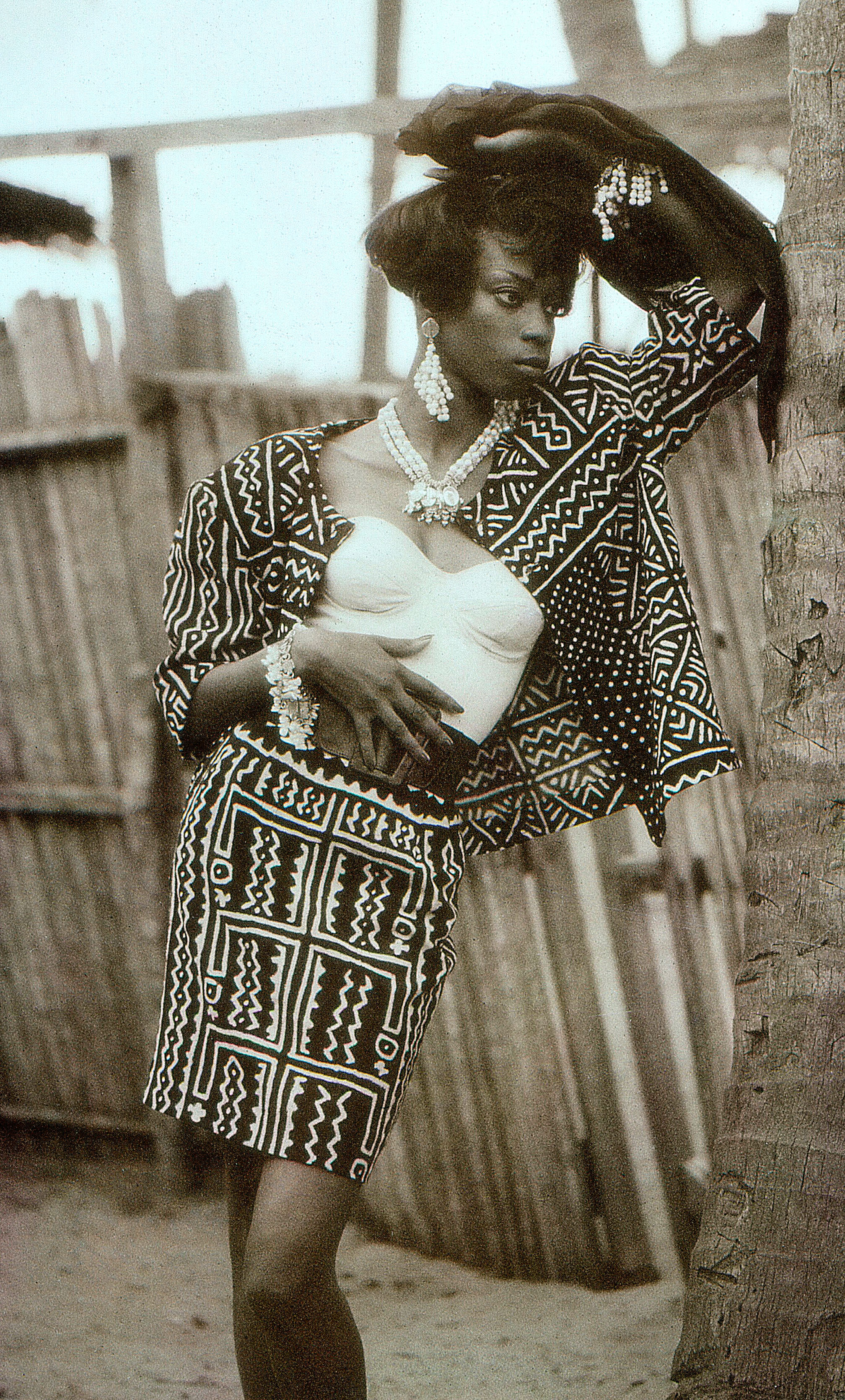 Black and white image of an African model wearing a matching skirt and shirt with African design, pearls and a white bandeau