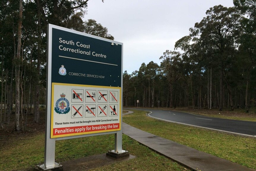 A sign emblazoned with 'South Coast Correctional Centre' stands in front of a winding bitumen road