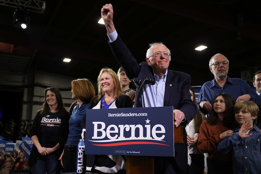 Bernie Sanders at a lectern with his fist in the air surrounded by family