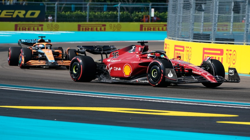 A Ferrari Formula 1 driver goes around a corner on the outside ahead of a Mclaren car.