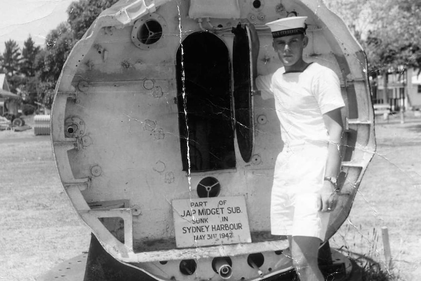 Young sailor on left in front of the back of a Japanese midget submarine with the door open.