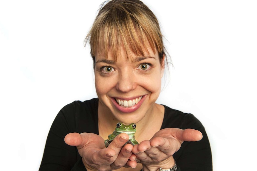 A smiling woman holding a green frog in her hands.