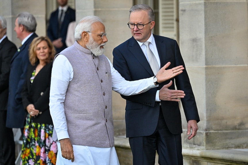 Two men wearing formal dress speak and gesture with their hands