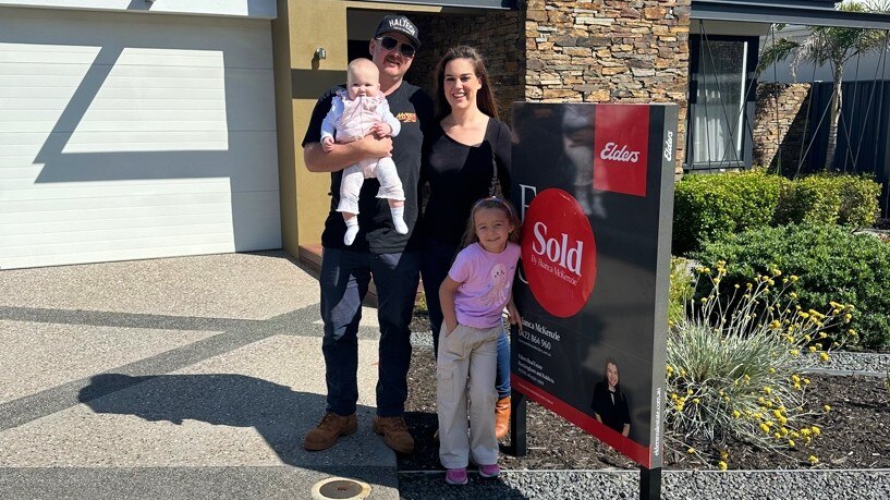 Una familia frente a una casa con un cartel de “Se vende”