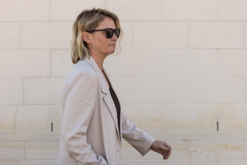A woman wearing a suit jacket leaving court wearing sunglasses.  