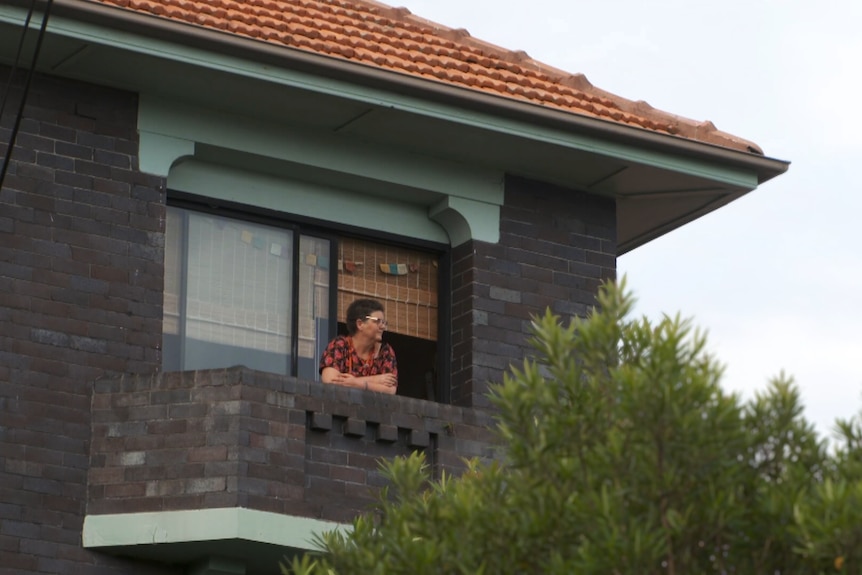 A woman looking out of the window of a dark brick house