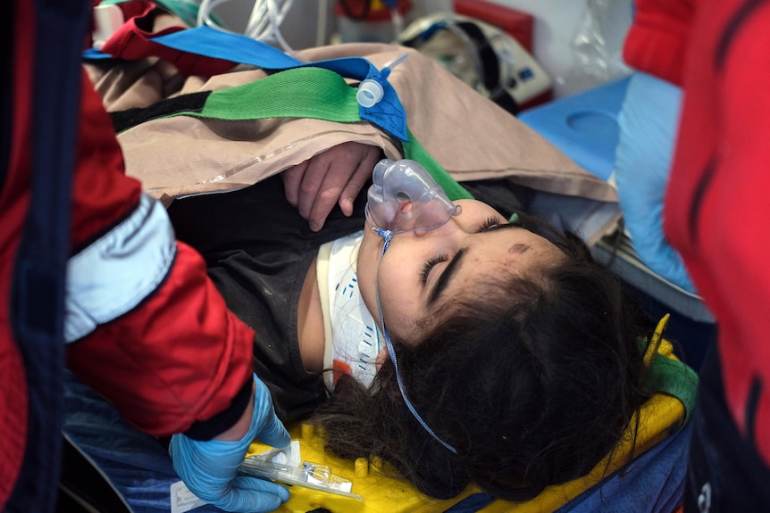 Close up of young girl with oxygen mask on lying on stretcher.