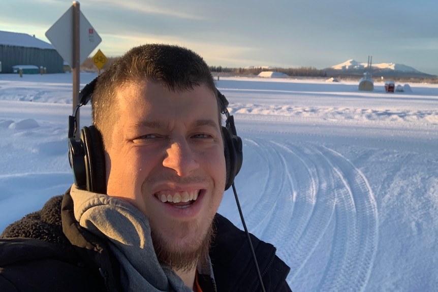 A man wearing headphones looking cold while outside in the snow.