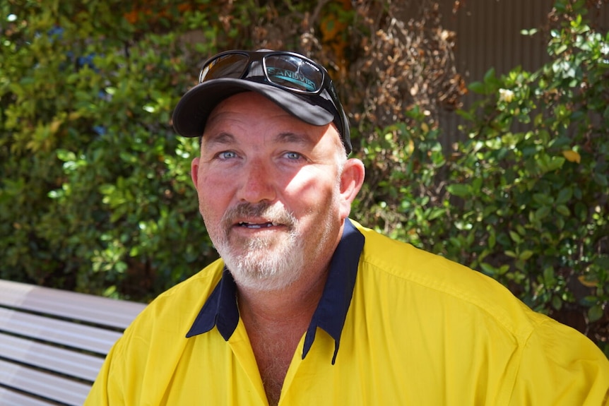 A man in yellow hi vis shirt, cap and sunglasses looks into the camera