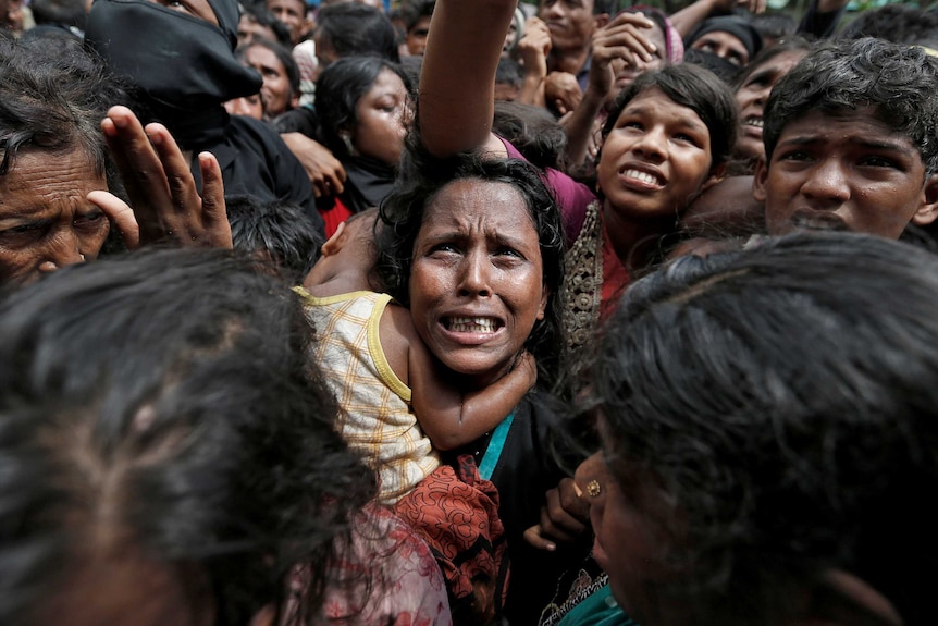 A woman, clutching a child, looks desperate in a crowd waiting for aid.