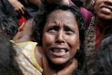A woman, clutching a child, looks desperate in a crowd waiting for aid.