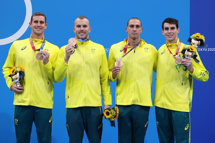 Four men in green and gold tracksuits hold bronze medals