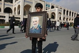 A boy is pictured in front of a classical Iranian building holding a portrait of Qassem Soleimani in a gilded bronze frame.