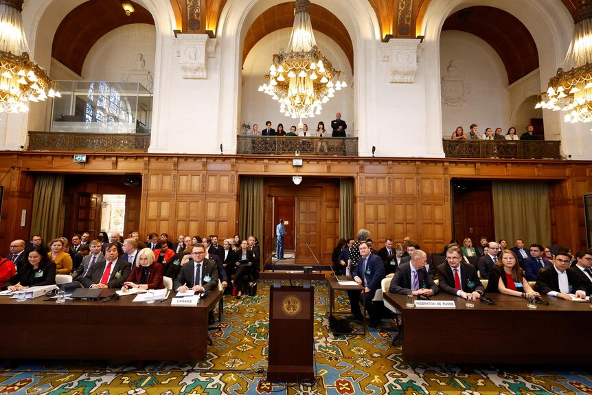 Court room with podium in centre and chandeliers hanging above ornate rug 