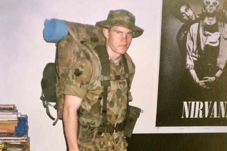 A photo of a man wearing a khaki suit posing in his bedroom.