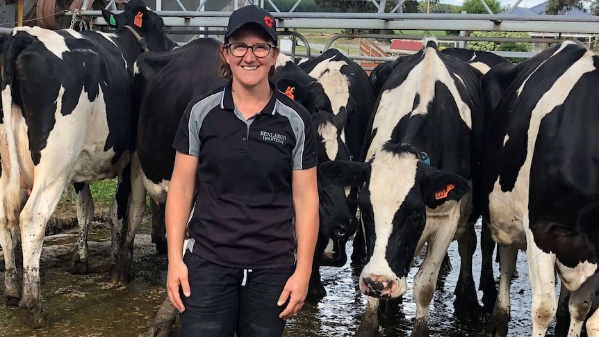 A woman wearing a t-shirt and hat stands in mud in front of black and white cows.