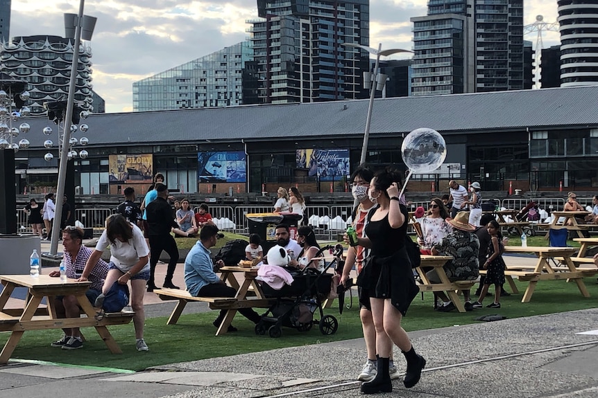 People walk past camera wearing masks in front of festival space 