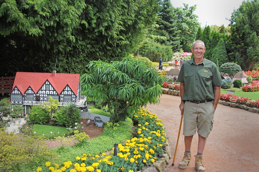 Man with a walking stick smiling next to a small scale building