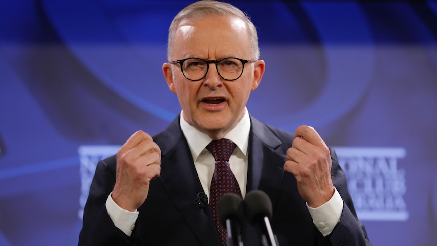 Anthony Albanese, a man wearing a black suit and dark spectacles, delivers a speech at a lectern with closed fists