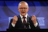 Anthony Albanese, a man wearing a black suit and dark spectacles, delivers a speech at a lectern with closed fists