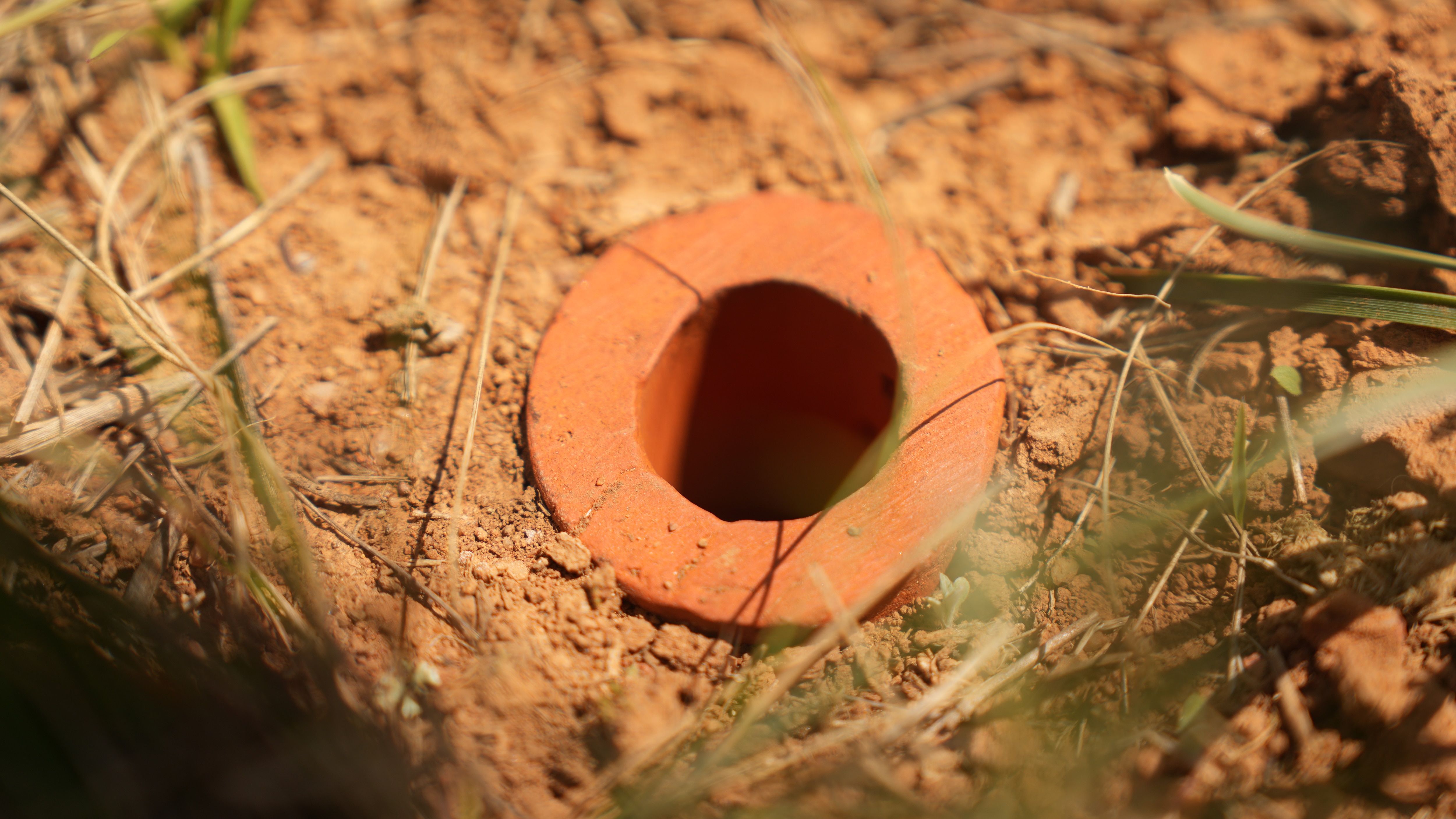 An open-ended terracotta pipe sticking out of a red dirt grassland.