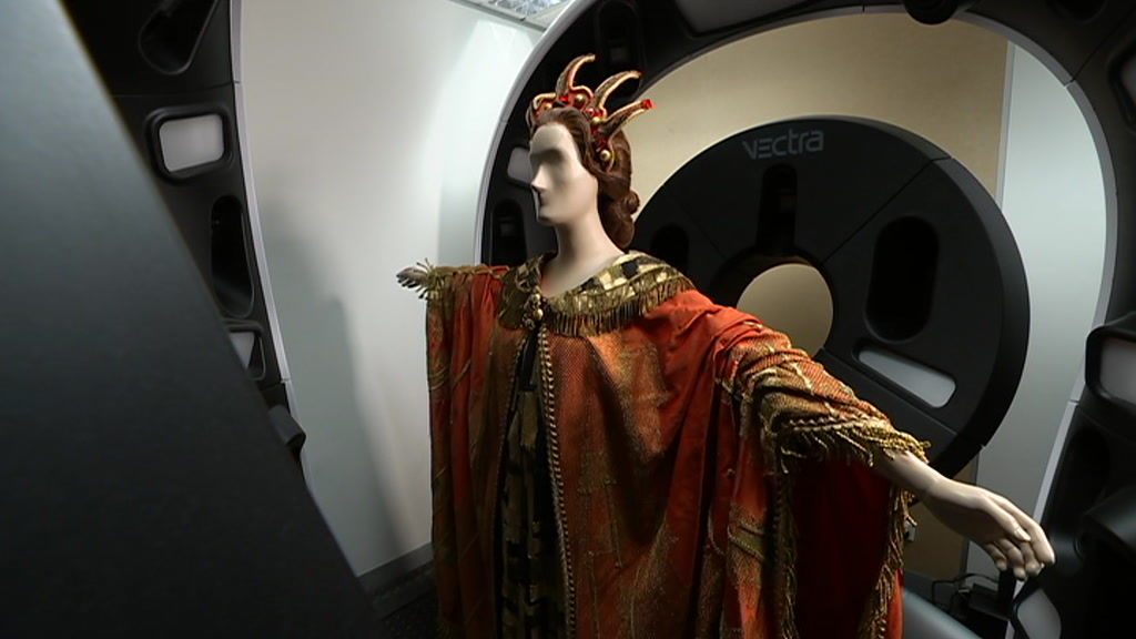 A mannequin with an orange opera costume is scanned in large medical scanner.