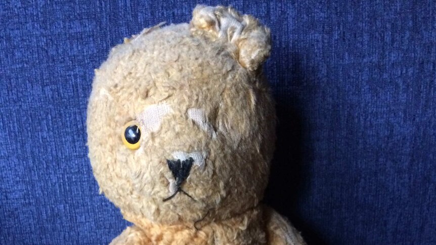 A worn teddy bear with one eye and one ear