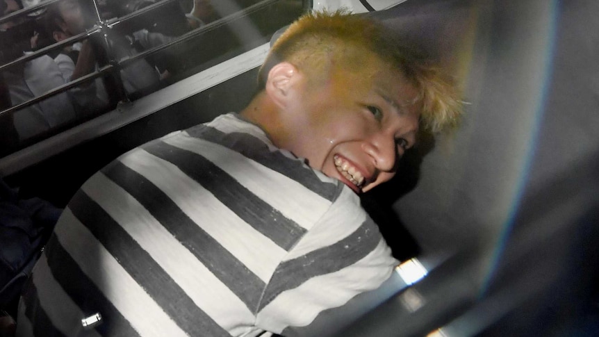 Satoshi Uematsu smiles widely inside a police car.