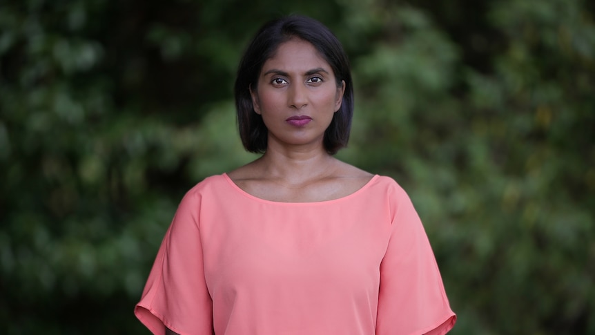 a woman in a pink top looks into the camera with a serious expression