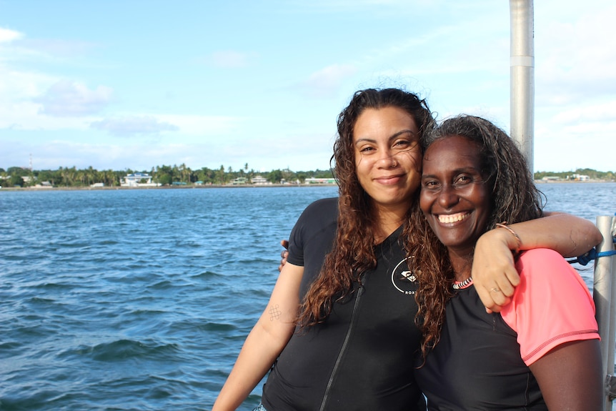 Dr Katy Soapi and Azaria Pickering hugging on the dive boat and smiling at the camera, their hair still wet