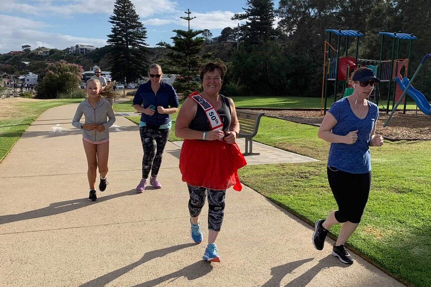 Diane Sinclair is pictured running among 3 other people at her 50th parkrun with a playground in the background