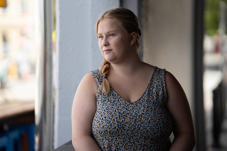 A young woman, Tara Payne, stands in a building archway and look out with a steady expression on her face.