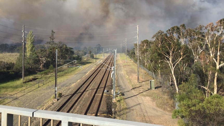 A large plume of smoke above two train tracks.