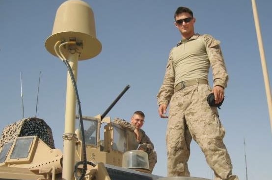 A man in military uniform stands on top of a military vehicle.