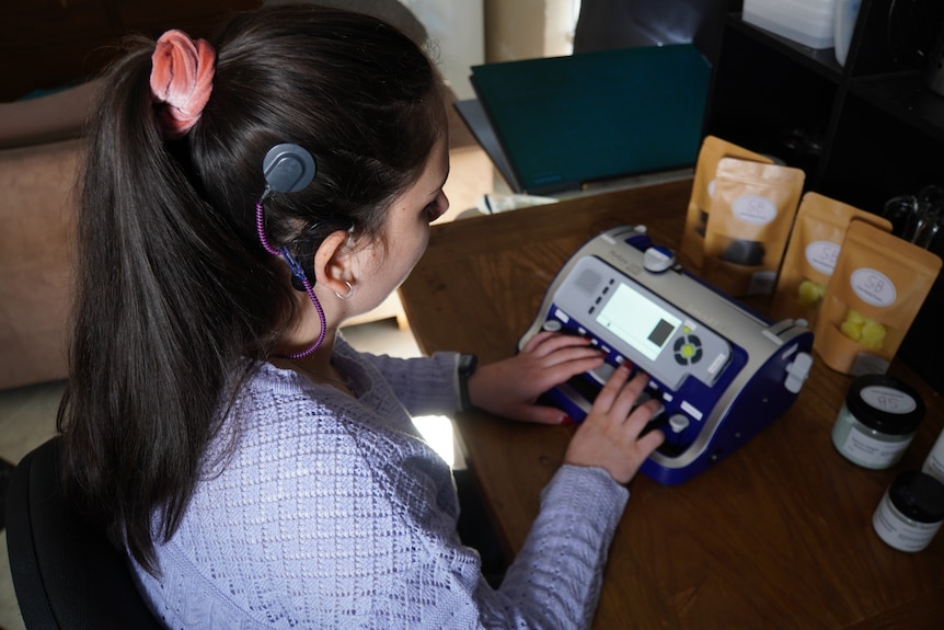 A woman in a violet jumper with a hearing aid. 