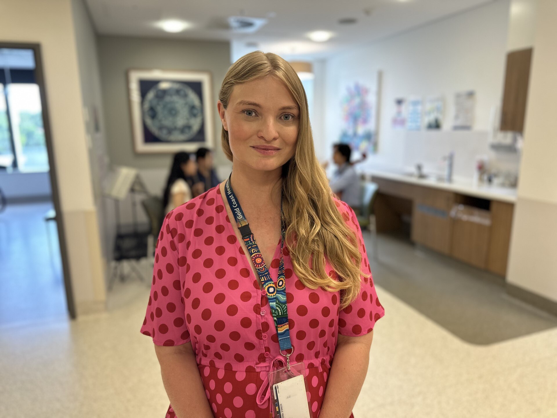 A blonde woman stands in a hospital corridor, smiling.