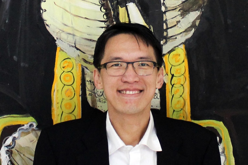A man in a suit and glasses smiles in front of a colourful backdrop