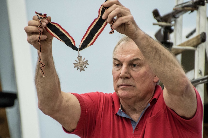 A man holds up a German war medal to show a crowd at an auction.