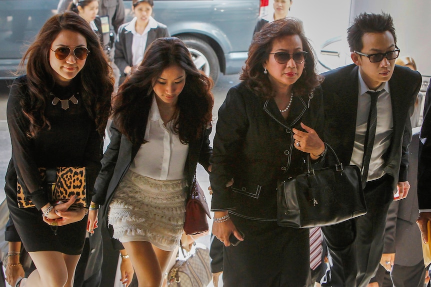 A glamorous family in dark-coloured clothes walks up stairs to a court.